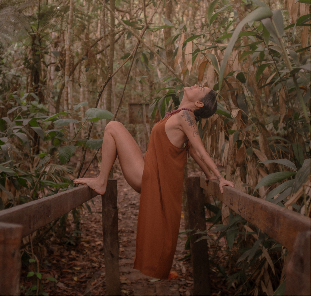 Kariny Elias em meio à mata, apoiada em uma ponte de madeira